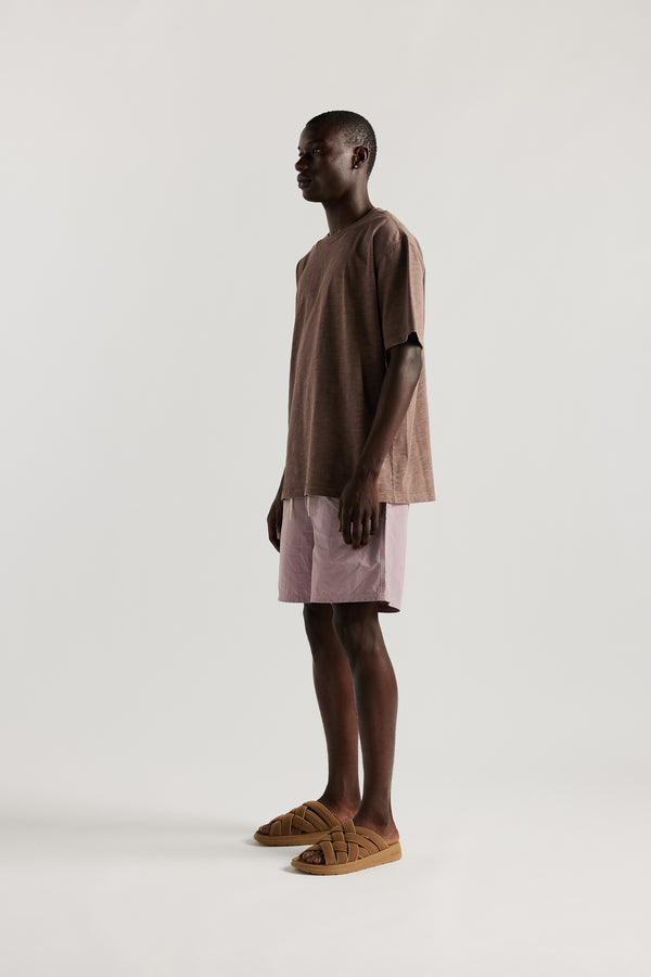 side view of Male model wearing relaxed fit swim shorts in lilac with an elastic drawstring waist and functional pocket detailing.