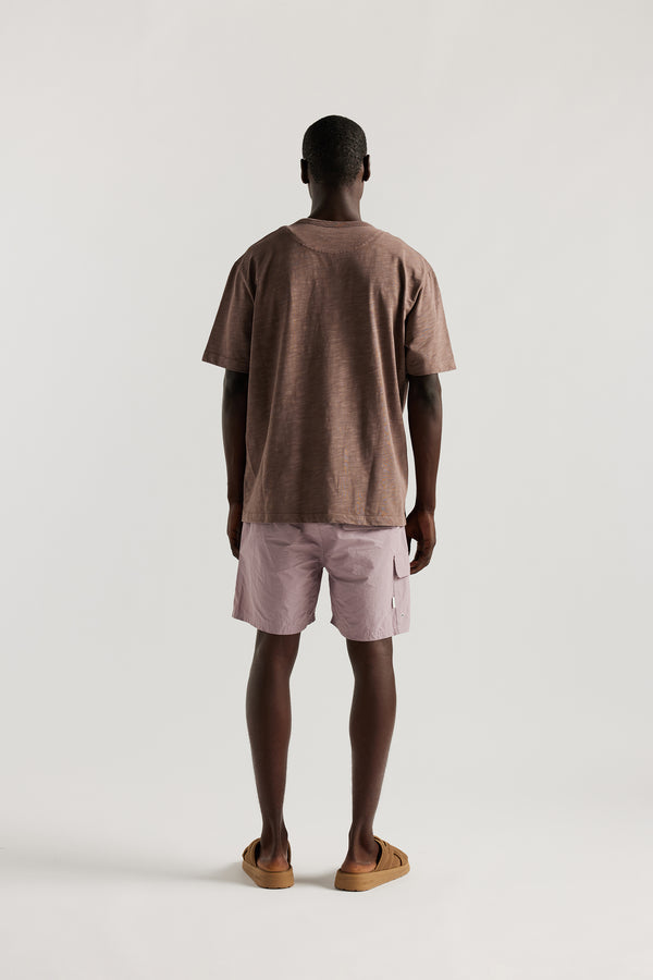 Back view of Male model wearing relaxed fit swim shorts in lilac with an elastic drawstring waist and functional pocket detailing.