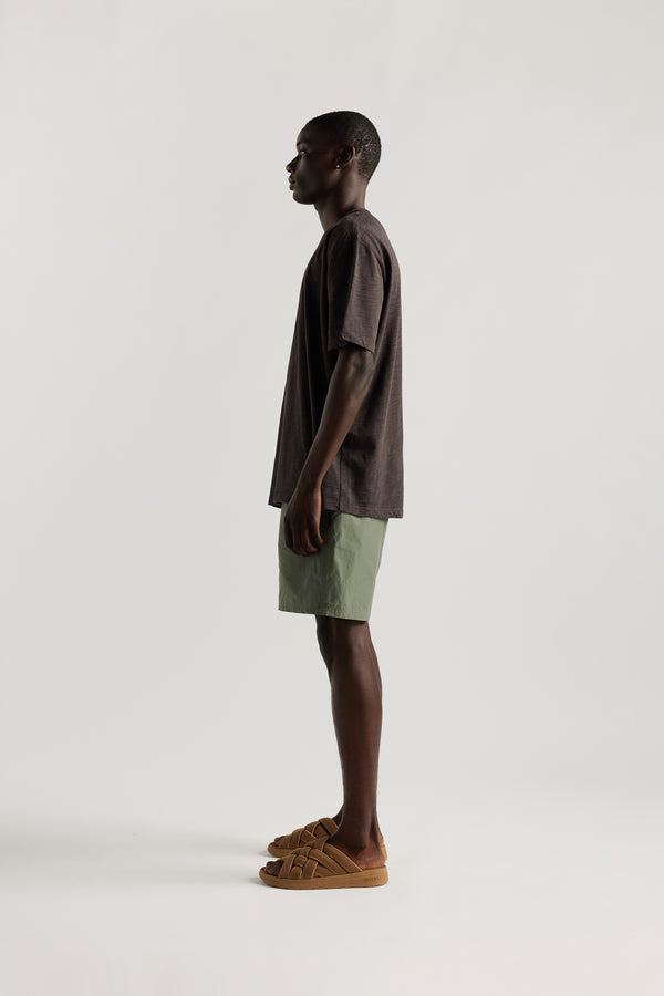 Side view of Male model wearing relaxed fit swim shorts in Olive green with an elastic drawstring waist and functional pocket detailing.