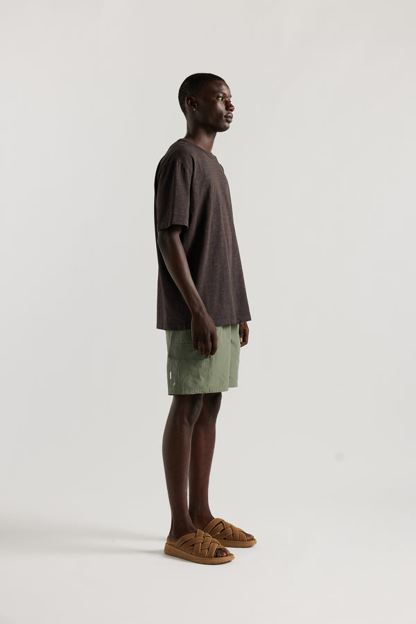 side view of Male model wearing relaxed fit swim shorts in Olive green with an elastic drawstring waist and functional pocket detailing.