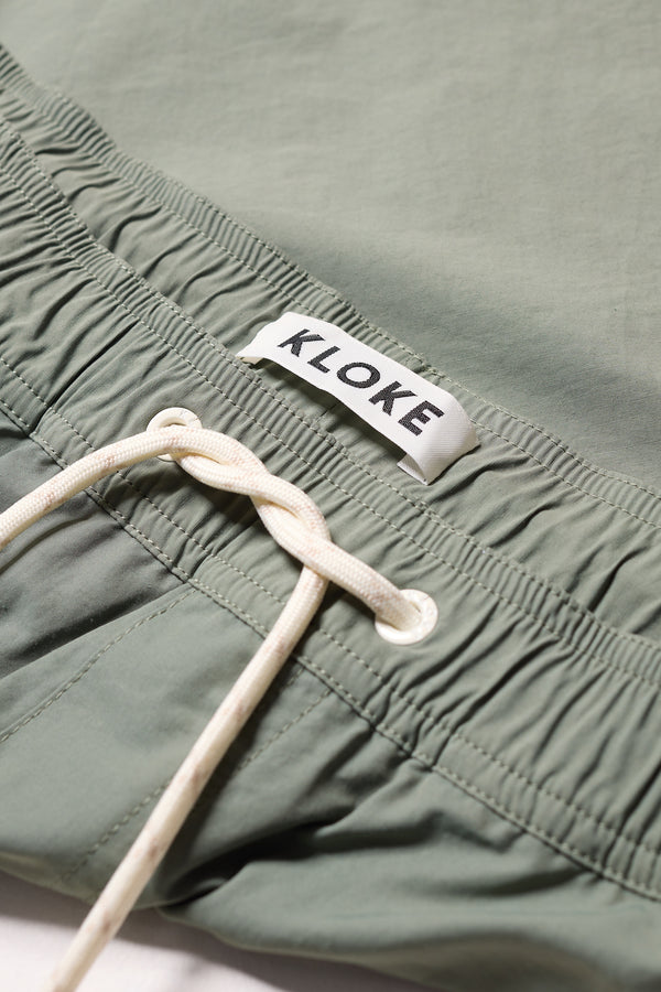close up detail shot of relaxed fit swim shorts in Olive green with an elastic drawstring waist and functional pocket detailing.