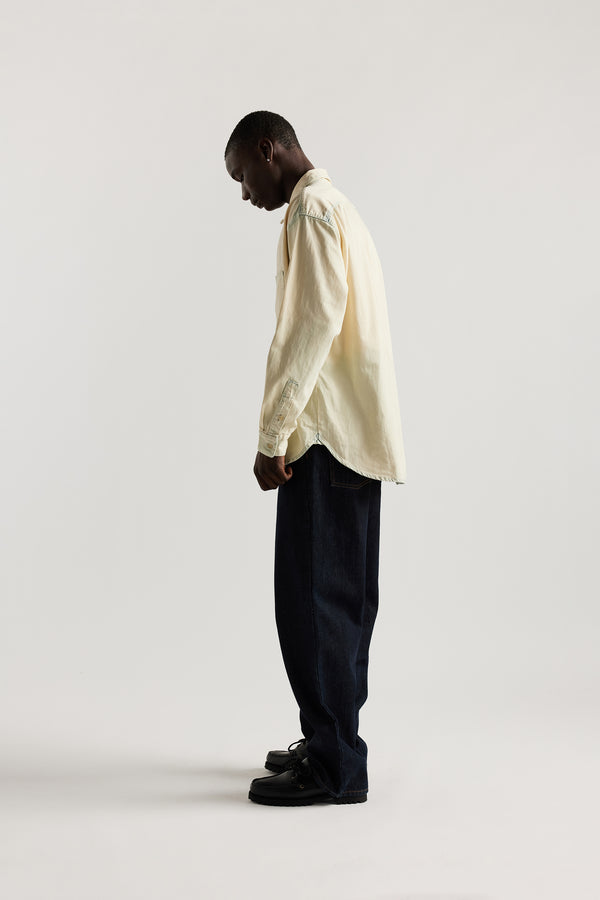 Side view of model in Mid blue Fade with Ecru tint Finite denim shirt showing rounded hem finished with bar tack detailing.