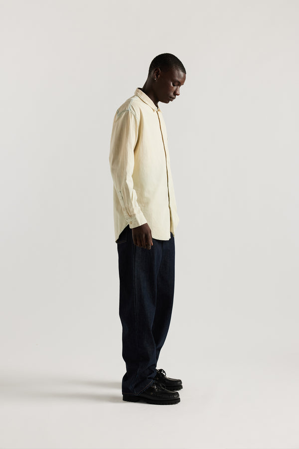 Side view of model in Mid blue Fade with Ecru tint Finite denim shirt showing rounded hem finished with bar tack detailing.