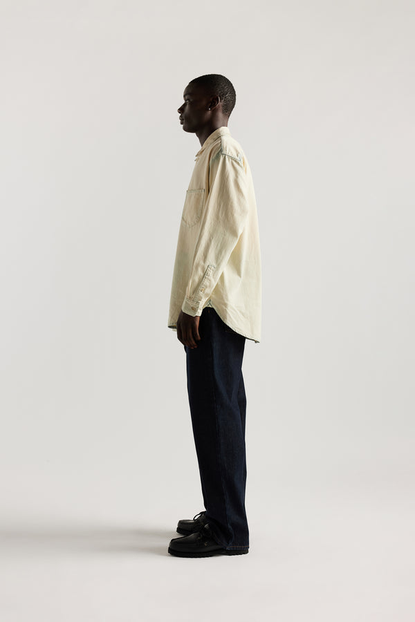 Side view of model in Mid blue Fade with Ecru tint Finite denim shirt showing rounded hem finished with bar tack detailing.