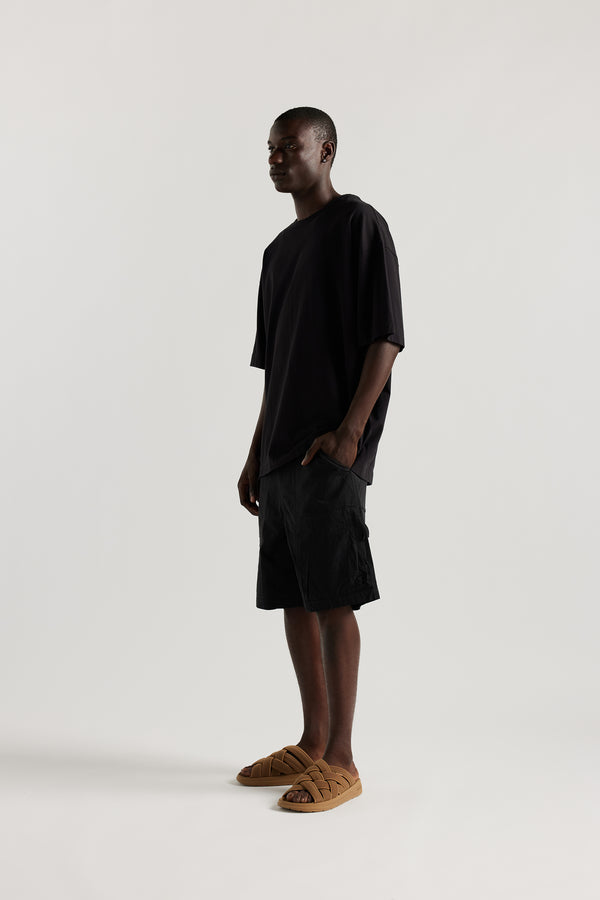 Side view of Ousmane in relaxed fit men’s cotton shorts in black showcasing 3D pocket construction, panel detailing, and structured laid-back design