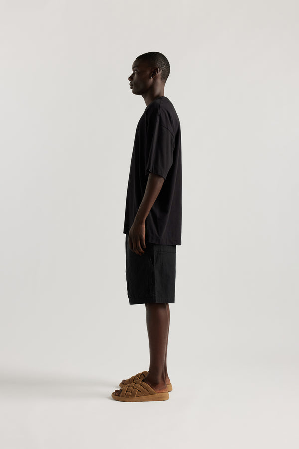 Side view of Ousmane in relaxed fit men’s cotton shorts in black showcasing 3D pocket construction, panel detailing, and structured laid-back design