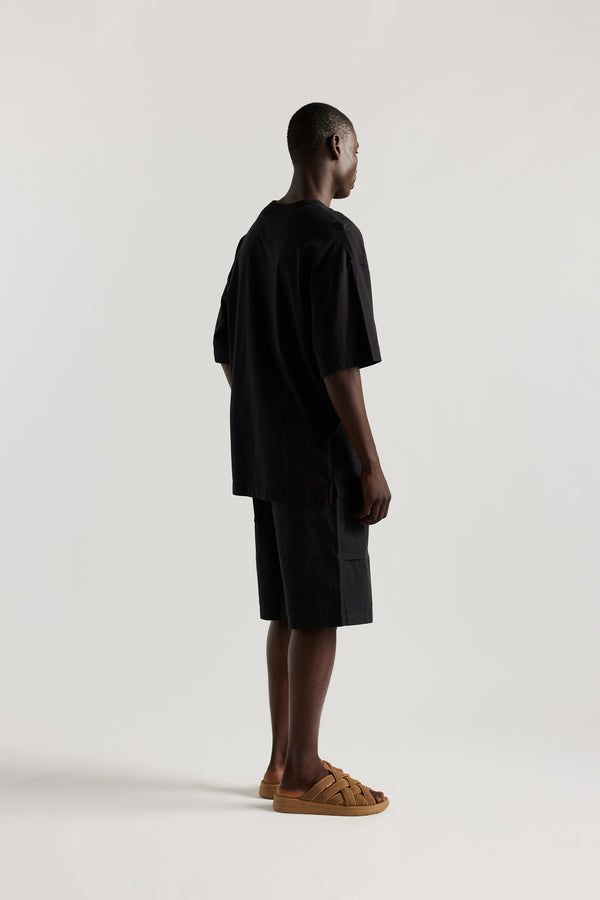 back view of Ousmane in relaxed fit men’s cotton shorts in black showcasing 3D pocket construction, panel detailing, and structured laid-back design