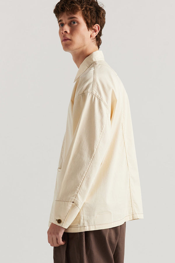 Side of male model wearing the Ecru Protocol Coverall in light 100% cotton denim. 