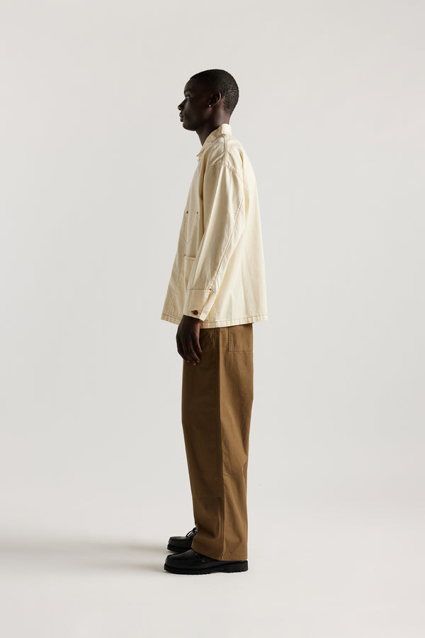 Side of male model wearing the Ecru Protocol Coverall in 100% cotton denim. 