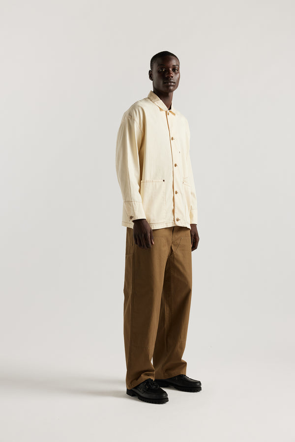 Side of male model wearing the Ecru Protocol Coverall in light 100% cotton denim. 