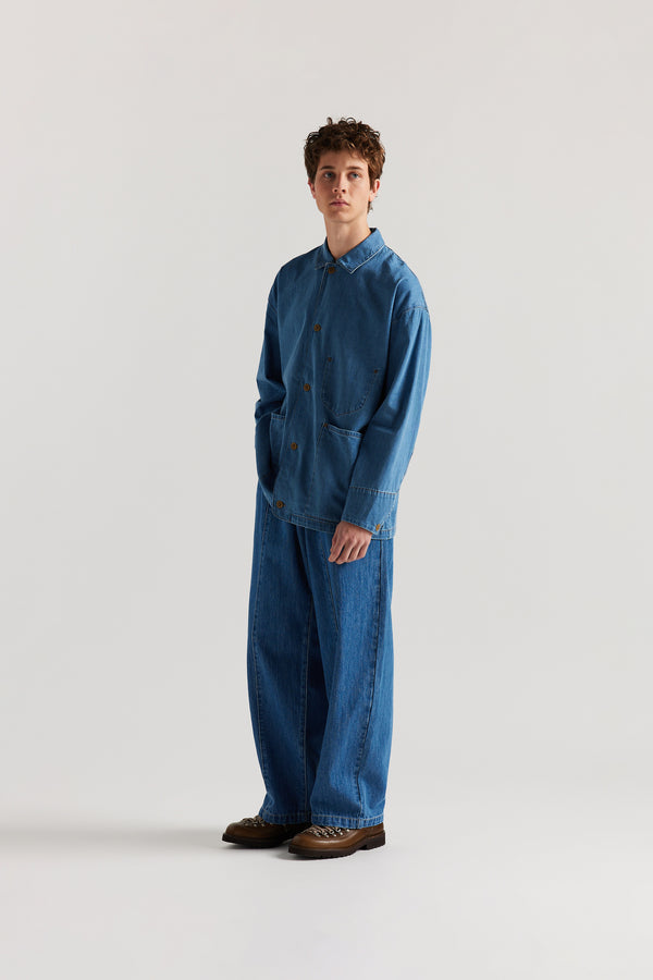 Front of male model wearing the Mid Wash Protocol Coverall in light 100% cotton denim, showing multiple patch pockets and built-in collar.
