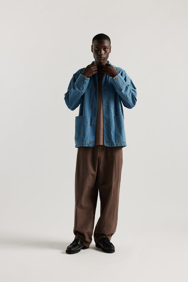 Front of male model wearing the Mid Wash Protocol Coverall in light 100% cotton denim, showing multiple patch pockets and built-in collar.