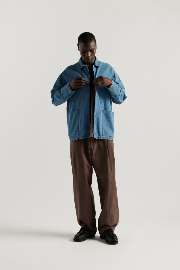 Front of male model wearing the Mid Wash Protocol Coverall in light 100% cotton denim, showing multiple patch pockets and built-in collar.