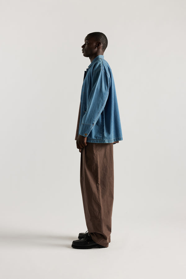 Front of male model wearing the Mid Wash Protocol Coverall in light 100% cotton denim, showing multiple patch pockets and built-in collar.