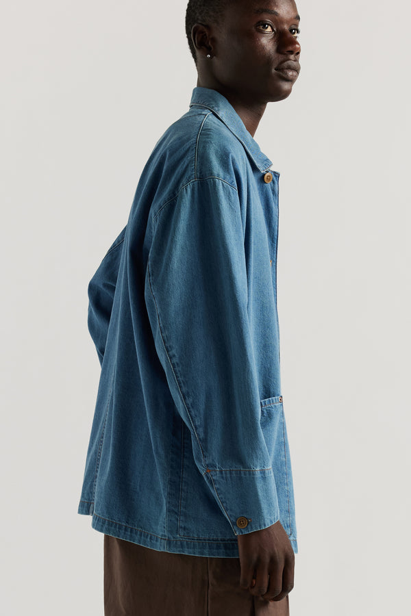Front of male model wearing the Mid Wash Protocol Coverall in light 100% cotton denim, showing multiple patch pockets and built-in collar.