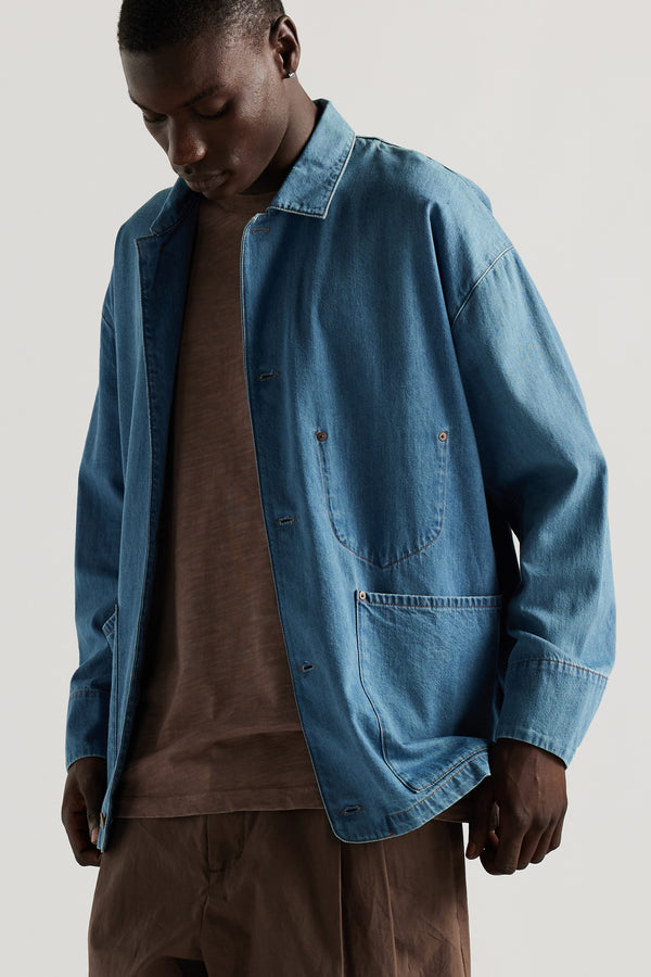 Front of male model wearing the Mid Wash Protocol Coverall in light 100% cotton denim, showing multiple patch pockets and built-in collar.