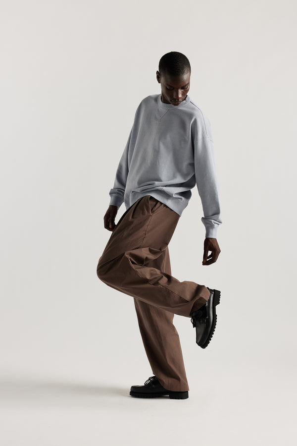 Oversized unisex French terry sweater in pigment-dyed finish, shown on model with relaxed dropped shoulders and flatlock seam detailing.
