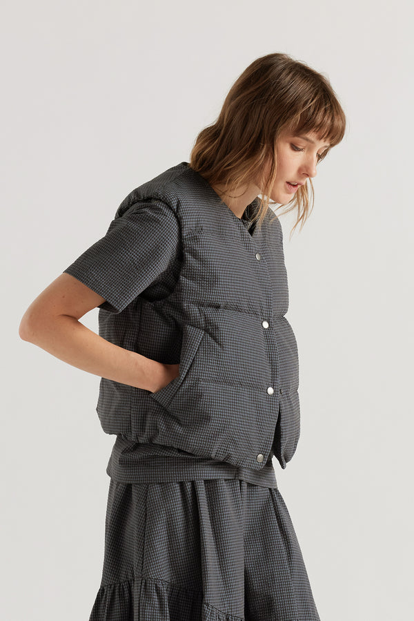 Front of the model in the blue Static Quilted Down Vest in Kloke's signature seersucker gingham with a V-neck, snap-front closure and front welt pockets.