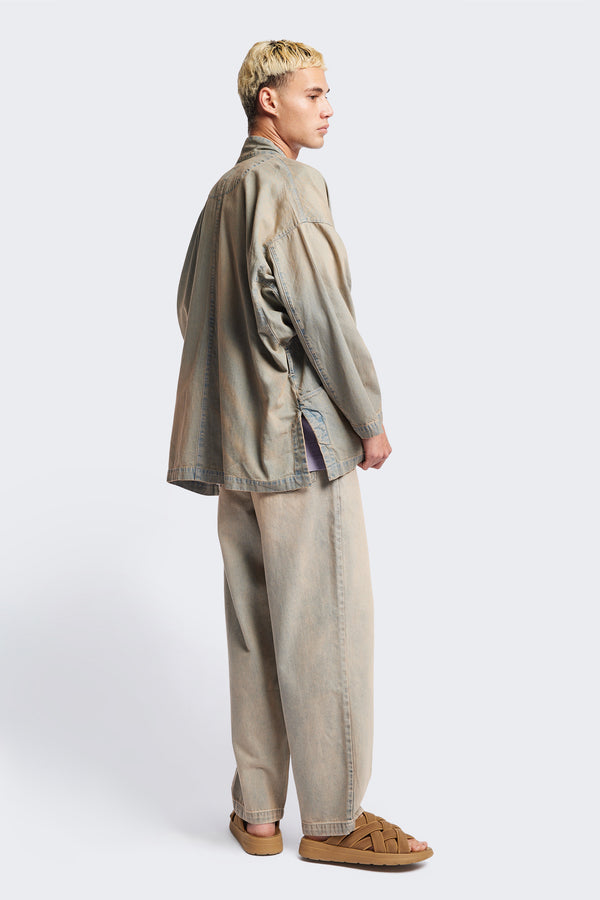 Side of the unisex Subterra Wide wrap shawl collar jacket with kimono-style sleeves, crafted from cotton denim, featuring front patch pockets and a waist tie to cinch the loose silhouette. Available in 5 sizes.  