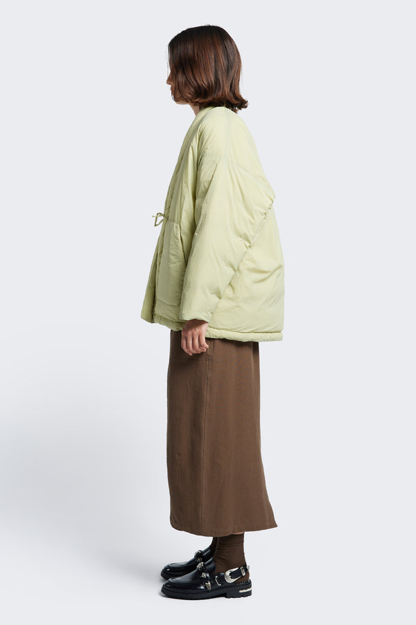 Model standing side on in the Abeyance Quilted Wrap Coat Sand, a Kimono style puffer jacket with a bagged out construction.