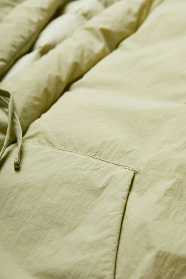 The Abeyance Quilted Coat Sand with centre front self tie and two patch pockets. Made from 100% Recycled Nylon, Lining 100% Recycled Nylon, Fill 100% Post Consumer Down Fill.