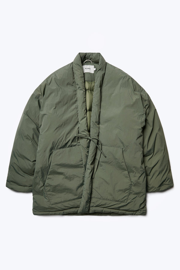 Flat lay of the Abeyance Quilted Coat Olive, a Kimono style puffer jacket with centre front self tie, two patch pockets and under arm gusset for comfort. 