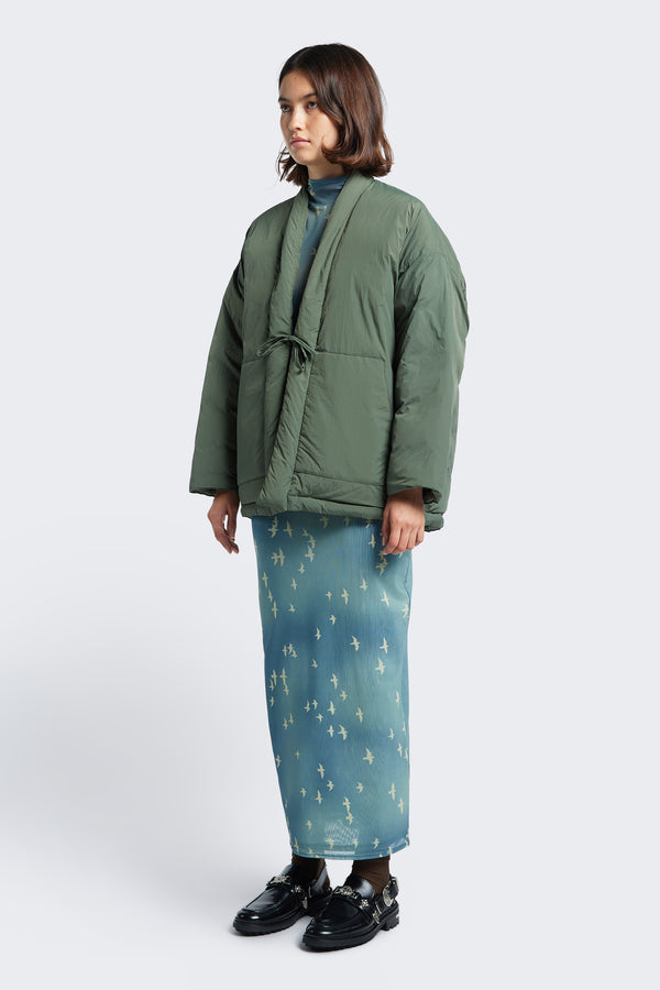 Model wearing the Abeyance Quilted Wrap Coat Olive, a kimono style puffer jacket with front centre self tie and two front patch pockets. 