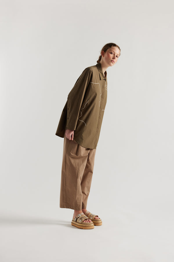Olive green/brown Ache Embroidered Shirt side view on female model, with embroidered motifs, long sleeves, and built-in collar