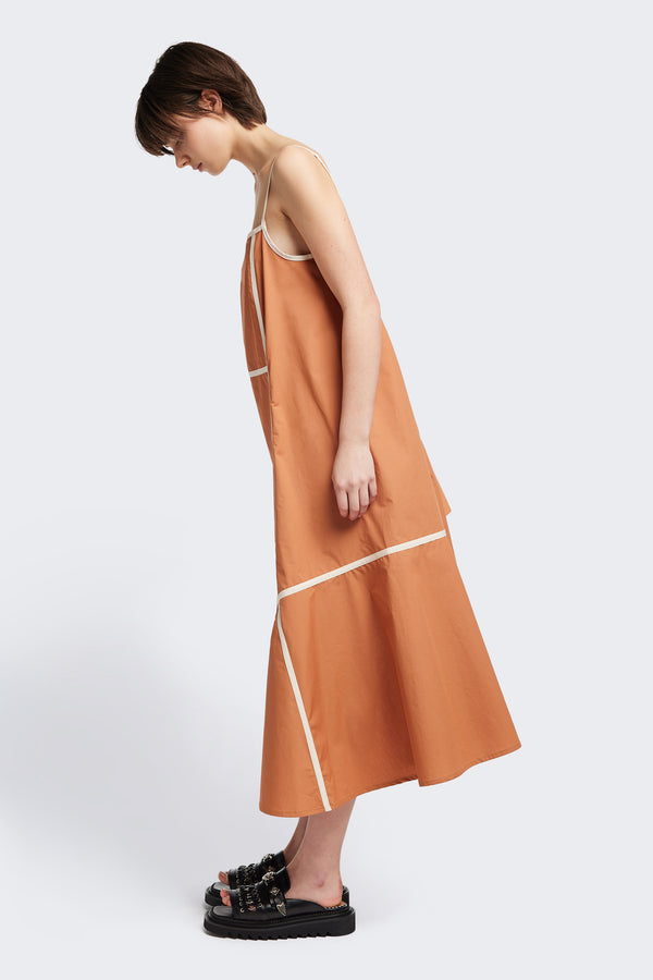 Side of the Adjourn Dress in burnt orange/ecru, featuring contrasting block colours, bound seam details, adjustable thin straps, a straight neckline, and a flared A-line skirt. Available in 5 sizes. 