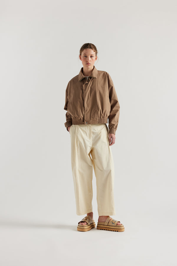 Front of the model in the Ecru Amber Pant. A Semi-tailored tapered pant with pleat waistband detail and front seam topstitching.