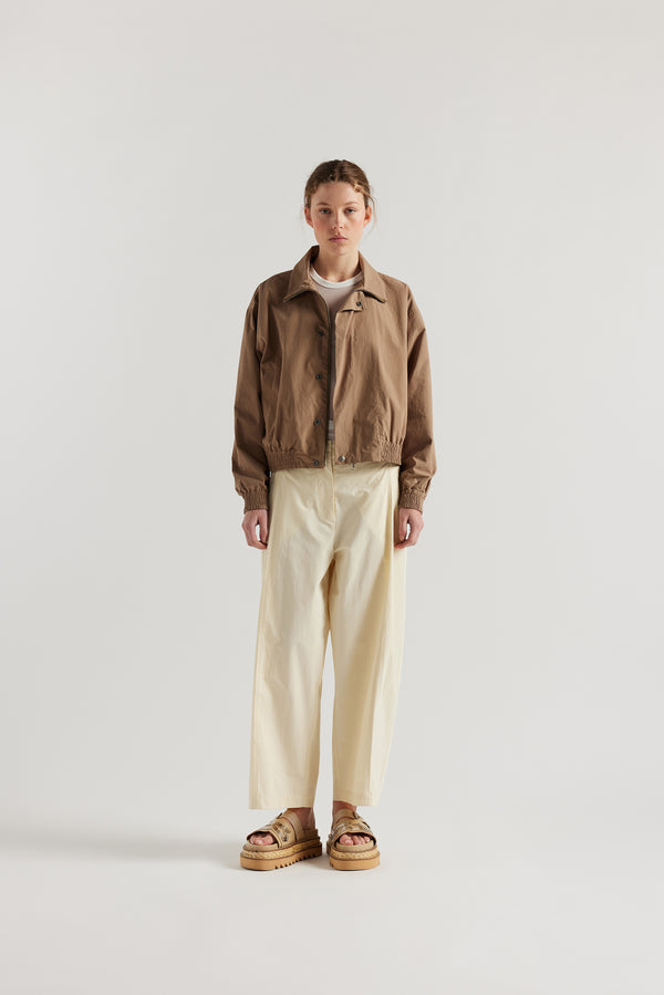 Front of the model in the Ecru Amber Pant. A Semi-tailored tapered pant with pleat waistband detail and front seam topstitching.