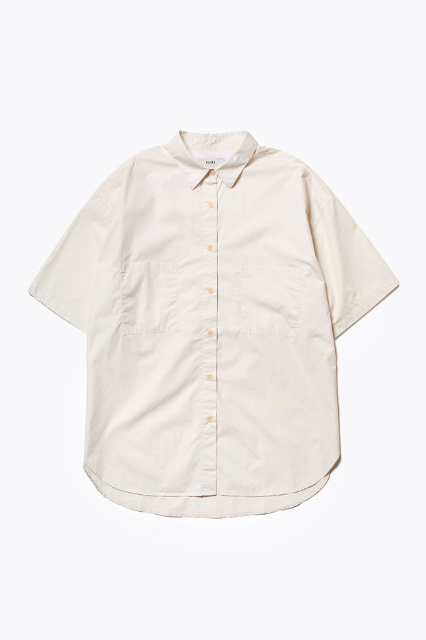 Flat Front of the Aquifer, a relaxed loose-fitting boxy short-sleeve shirt with back button placket, scoop hemline, and chest patch pockets, crafted in lightweight cotton poplin. Available in 5 sizes. 