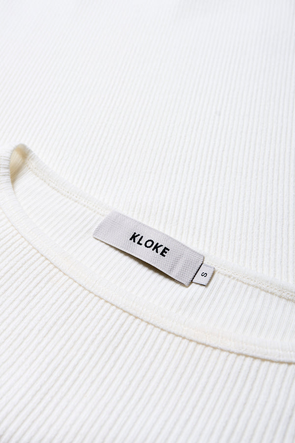 Close up details of the arbour top, a slim-fitting t-shirt-style top, in off white. With a boat neckline and single bind trim, made from fine Japanese rib knit with slight stretch, perfect for casual and stylish outfits