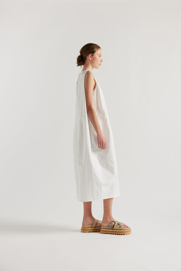 Side view of female model in the white  Aureole Dress front view showing panelled detailing and relaxed skirt with front inseam split