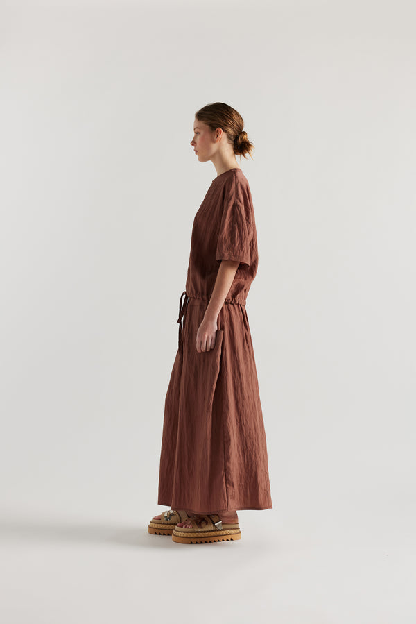 Side of Model in the brown Calm Skirt with panelled construction, scoop pockets and elasticated drawcord waistband in lightweight textured fabric.