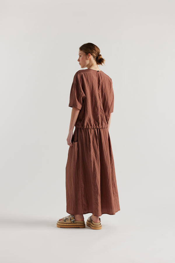 Back of Model in the brown Calm Skirt with panelled construction, scoop pockets and elasticated drawcord waistband in lightweight textured fabric.