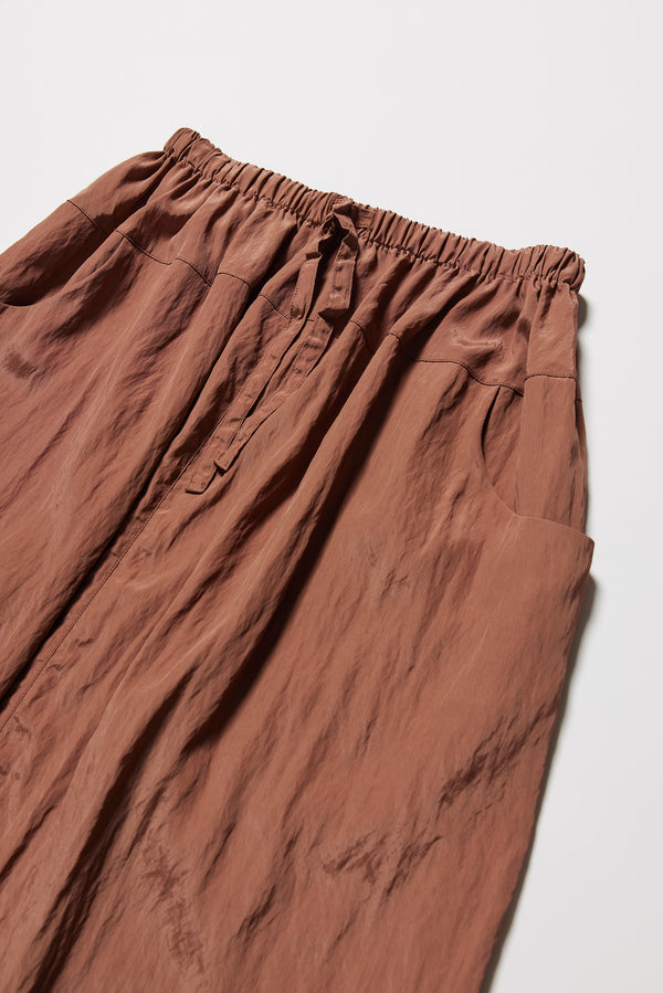 Close up detail shot of the brown Calm Skirt with panelled construction, scoop pockets and elasticated drawcord waistband in lightweight textured fabric.