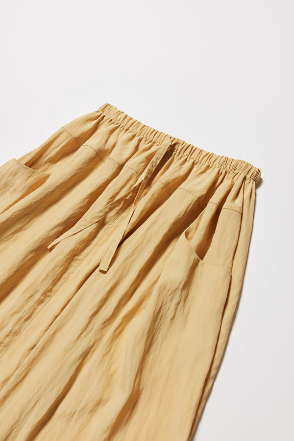 Close up detail shot of the beige Calm Skirt with panelled construction, scoop pockets and elasticated drawcord waistband in lightweight textured fabric.