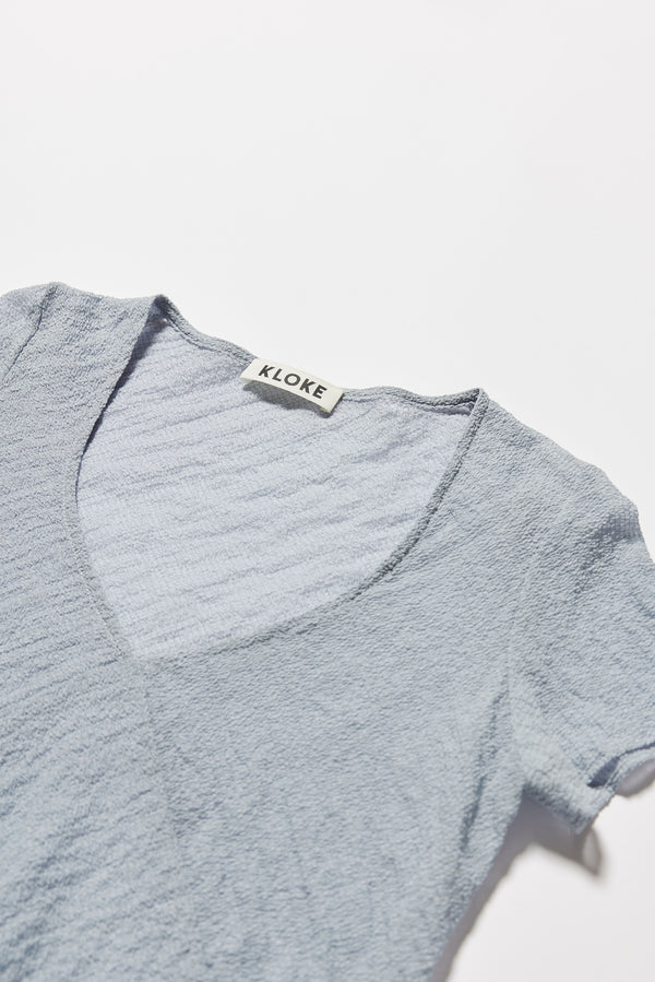 Close-up of sheer textured fabric in pale blue and V-neckline detail on slim-fit cap sleeve top.