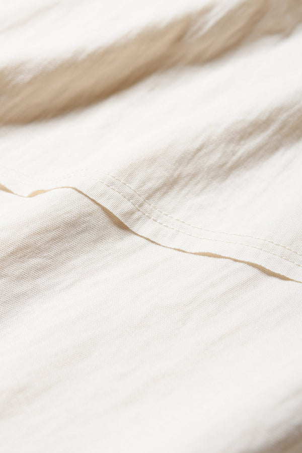 Close up fabric details of the Chaise top in Ecru, a relaxed crew-neck top in a Japanese rayon blend with short sleeves, boxy fit, raw hemline, and exposed seam detail across the mid-back.