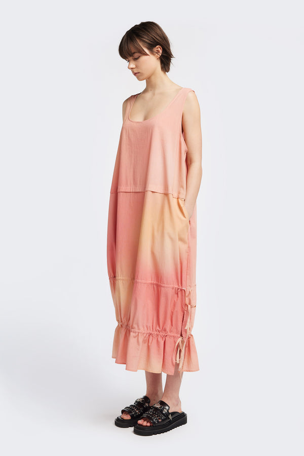 A female model wearing a sleeveless, cloud print, maxi dress in shades of and pink with a scoop neckline and wide shoulder straps. The dress features a adjustable drawstring details.