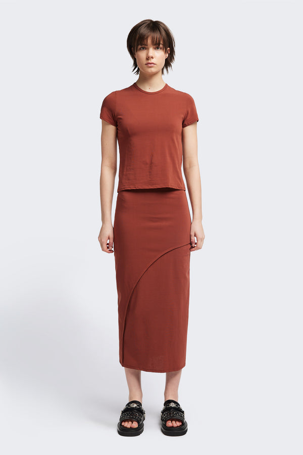 Front view of The Cumulus Skirt in brick red. A Slim, mid-calf dress in a cotton blend with stretch, featuring a curved bound seam for a flattering silhouette.