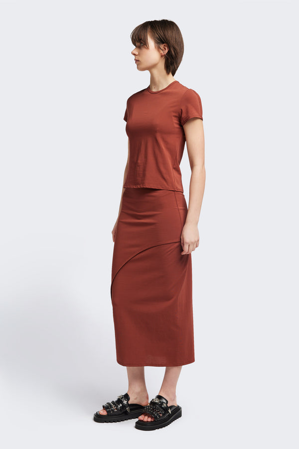 Front view of The Cumulus Skirt in brick red. A Slim, mid-calf dress in a cotton blend with stretch, featuring a curved bound seam for a flattering silhouette.