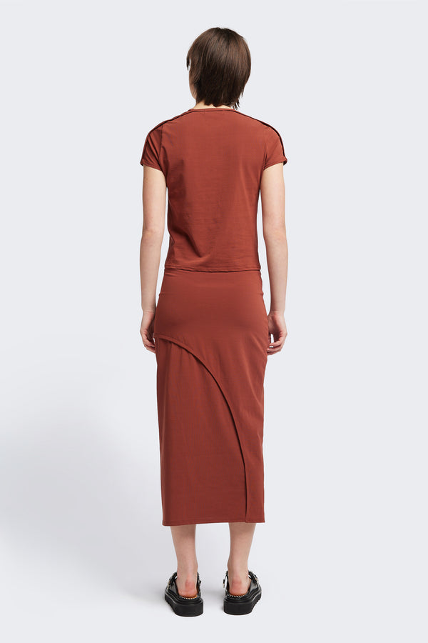 Back view of The Cumulus Skirt in brick red. A Slim, mid-calf dress in a cotton blend with stretch, featuring a curved bound seam for a flattering silhouette.