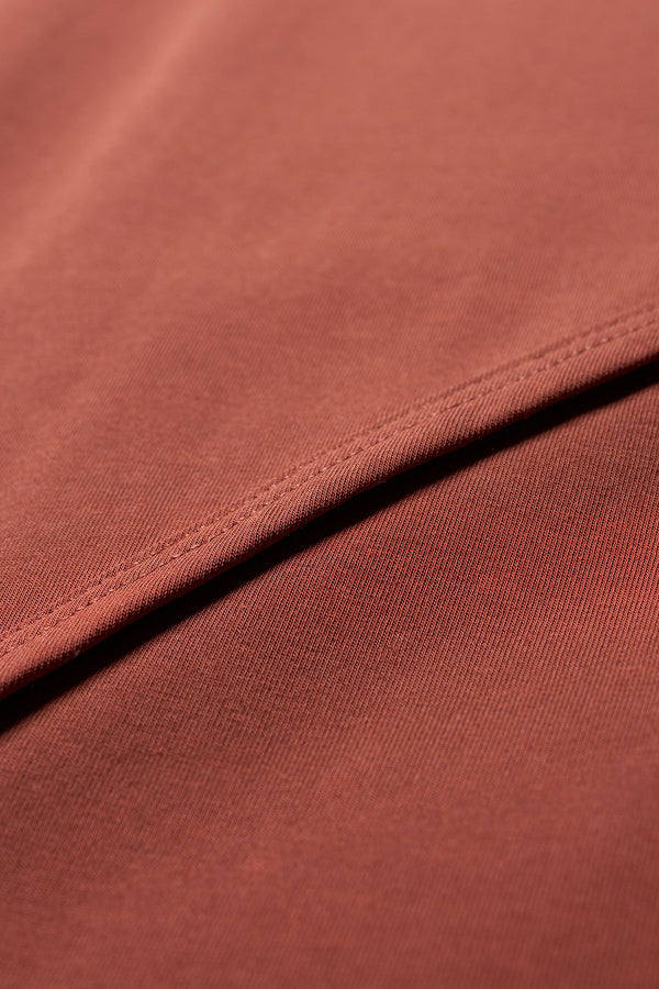 Close up fabric view of The Cumulus Skirt in brick red. A Slim, mid-calf dress in a cotton blend with stretch, featuring a curved bound seam for a flattering silhouette.