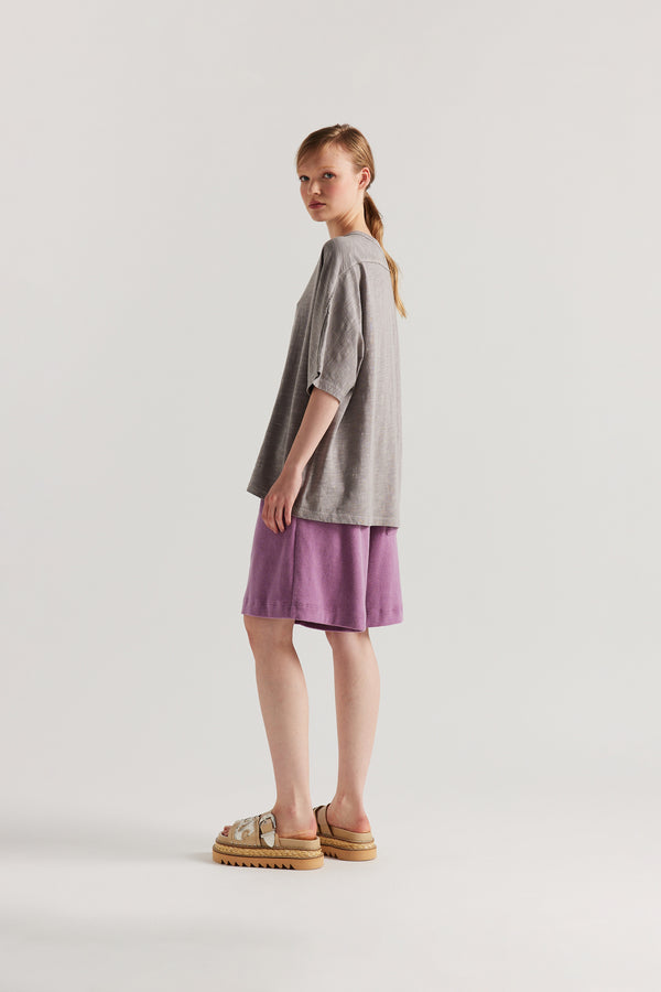 Back view of model in the Mauve Declare Tee in pigment-dyed slub cotton with relaxed boxy fit - highlighting the overlocked seam detailing. 