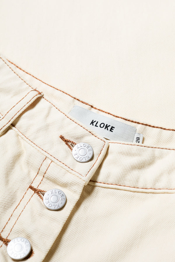 Close up of the Delphi Jean in ecru, featuring a wide leg that tapers at the ankle, with an exposed button fly and Kloke-branded hardware. Available in 10 sizes. 