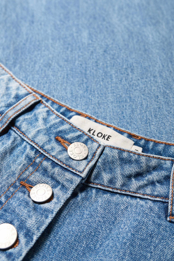 Close up of the Delphi Jean in mid blue fade, featuring a wide leg that tapers at the ankle, with an exposed button fly and Kloke-branded hardware. Available in 10 sizes. 