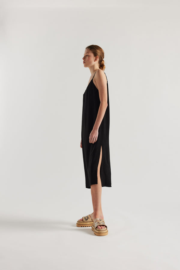 Side view of model in black Mid-length slip dress with straight neckline and relaxed silhouette