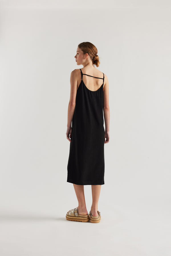 Back view of model in black Mid-length slip dress with straight neckline and relaxed silhouette